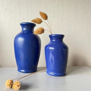 Peut inclure: Deux vases en céramique bleus de tailles différentes. Le grand vase est plus grand et plus large que le petit vase. Les deux vases ont un glaçage bleu moucheté.
