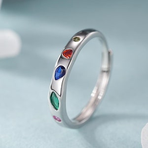 May include: A silver ring with five colorful gemstones set in a row. The gemstones are red, green, blue, pink, and orange.