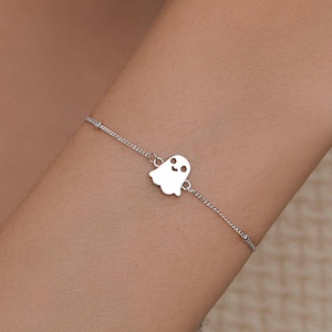May include: A delicate silver bracelet with a ghost charm. The charm is a small, smiling ghost with a rounded body and simple features. The bracelet is made of a fine chain and is a simple, elegant design.