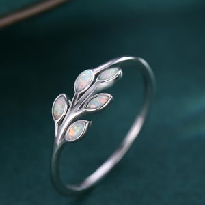 Könnte beinhalten: Ein silberner Ring mit einem zarten Zweigdesign mit Opal-Steinen. Der Ring liegt auf einem grünen Hintergrund.