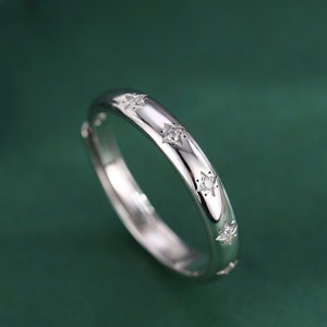 May include: A silver band ring with small, clear stones set in a star shape around the band.