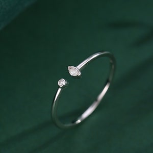 May include: A silver ring with two small, clear gemstones. The ring is open on one side and has a marquise-shaped stone on the other side.