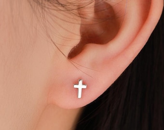 May include: A close-up of a person's ear with a small silver cross stud earring.