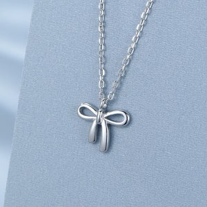 Op de afbeelding: Een zilveren ketting met een delicate strik hanger. De ketting ligt op een lichtblauwe achtergrond met een waterdruppel logo met de tekst "SRS".