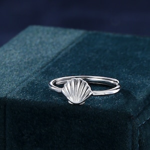 May include: A silver ring with a seashell design. The ring is on a dark green velvet box.