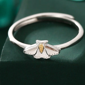 May include: A silver ring featuring a gold butterfly design. The ring is displayed on a green surface.