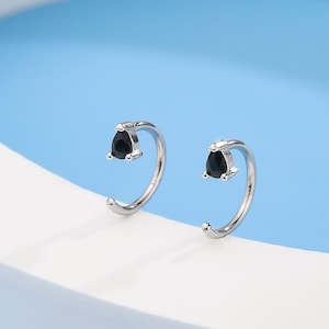 May include: A pair of silver hoop earrings with a small black gemstone set in each hoop.