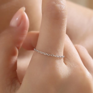 May include: A delicate silver chain ring worn on a finger.