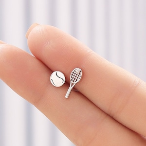 Può includere: Un paio di orecchini in argento a tema tennis. Un orecchino presenta una racchetta da tennis e l'altro una pallina da tennis.