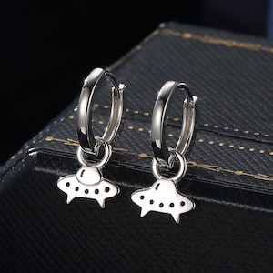 May include: A pair of silver hoop earrings with a small UFO charm hanging from each hoop.