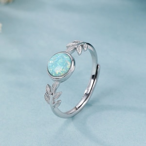Op de afbeelding: Een zilveren ring met een lichtblauwe opaal en delicate bladeren.