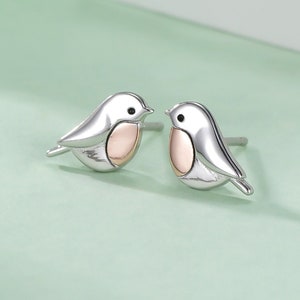 May include: A pair of silver earrings featuring a small robin design with a pink accent on the chest.