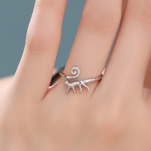 May include: A silver ring featuring a cat design. The cat's tail curls around the ring.