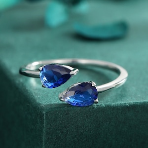 May include: A silver ring with two teardrop-shaped blue gemstones. The ring is on a green velvet surface.