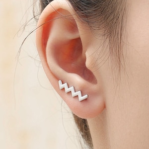 May include: A silver ear cuff with a zig-zag design. The cuff is worn on the upper part of the ear.