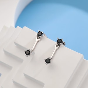 Puede incluir: Un par de pendientes de plata con piedras preciosas negras. Cada pendiente tiene una pequeña piedra preciosa en la parte superior y una piedra preciosa más grande que cuelga debajo.