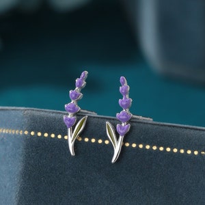 Puede incluir: Un par de pendientes de botón de plata con un diseño de flor de lavanda. Las flores son moradas y los tallos son verdes.