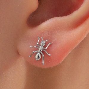 May include: A silver ant-shaped stud earring worn in a person's earlobe.