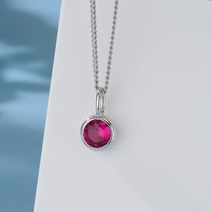 May include: A silver chain necklace with a small, round pendant featuring a bright red gemstone.