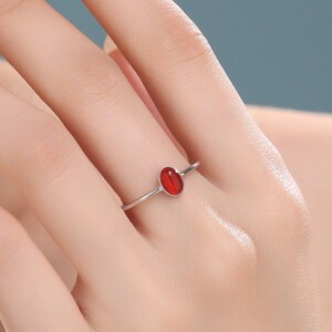 Op de afbeelding: Een zilveren ring met een rode ovale edelsteen. De ring zit aan een vinger.