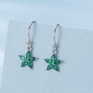 May include: A pair of silver dangle earrings with a green flower design. Each earring features a five-pointed star shape with green gemstones.