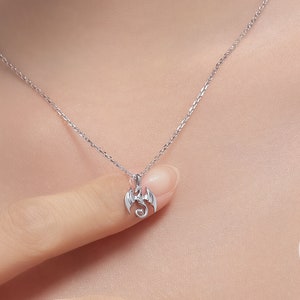 May include: A silver necklace with a small dragon pendant. The dragon is facing forward with its wings spread out.