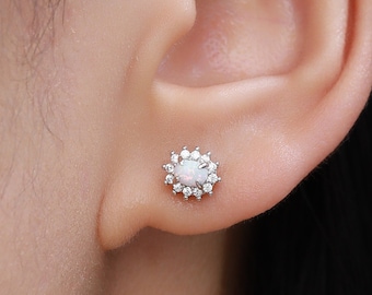Puede incluir: Primer plano de una oreja con un pequeño pendiente de plata con una opala blanca rodeada de un halo de pequeñas piedras transparentes.