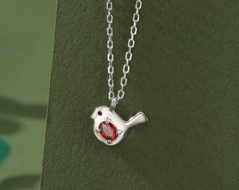 May include: A silver chain necklace with a small bird pendant. The bird has a red gemstone for its chest.