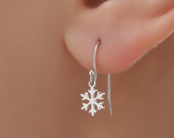May include: Silver snowflake dangle earrings with a delicate design. The earrings are shown on a person's ear.