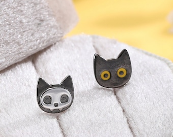 May include: A pair of silver cat-shaped stud earrings with black enamel and yellow eyes, displayed in a white velvet jewelry box.