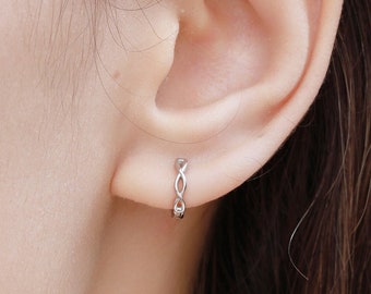 May include: A close-up of a person's ear with a small silver infinity symbol hoop earring. The earring is made of a delicate chain.