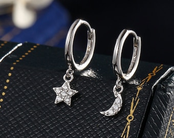 May include: A pair of silver hoop earrings with a dangling star and crescent moon charm. Each charm is adorned with small, clear cubic zirconia stones.