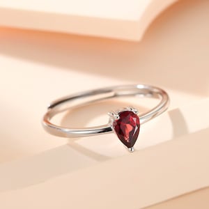 May include: A silver ring with a pear-shaped red gemstone.