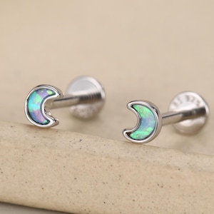 Può includere: Un paio di orecchini a lobo color argento a forma di mezzaluna con un inserto iridescente blu e verde. Ogni orecchino ha una chiusura circolare piatta e un perno, con il testo 925 chiaramente visibile sul retro del perno dell'orecchino.