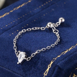 May include: A silver adjustable ring with a teardrop-shaped clear stone on a blue velvet background.