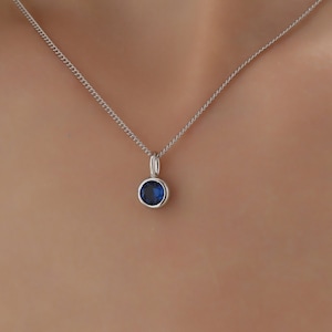 Puede incluir: Un collar de cadena de plata con un pequeño colgante redondo de piedra azul.