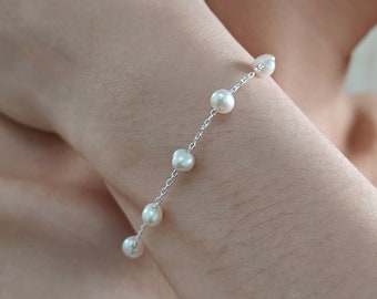 Peut inclure: Un bracelet délicat en chaîne argentée avec de petites perles blanches. Le bracelet est porté au poignet.