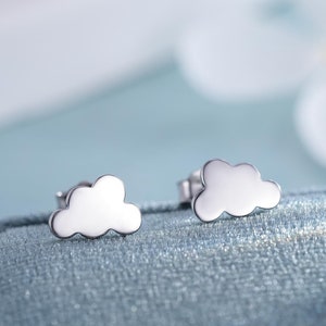 Puede incluir: Un par de pendientes de botón de plata en forma de nube. Los pendientes son pequeños y delicados, y son perfectos para el uso diario.