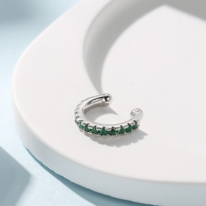 Op de afbeelding: Een zilveren oormanchet met een rij groene edelstenen.