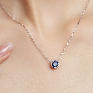 May include: A silver chain necklace with a small, round pendant featuring a dark blue gemstone.