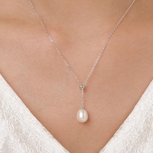 May include: A delicate silver necklace featuring a single, teardrop-shaped pearl pendant. The pearl hangs from a fine chain, with a small silver bead accentuating the design. The necklace is displayed against a white background.