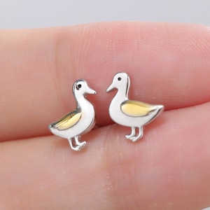 May include: A pair of silver stud earrings featuring a small duck design. The ducks are white with yellow accents.
