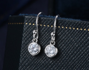 May include: A pair of silver dangle earrings with clear round cubic zirconia stones. The earrings are in a black jewellery box.