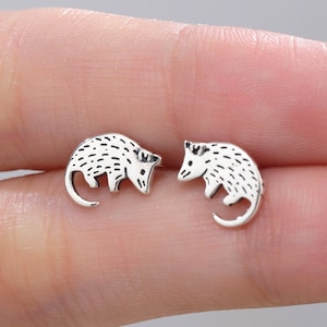 May include: A pair of silver opossum stud earrings. The opossums are facing each other and have a detailed design.