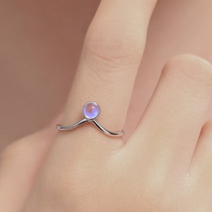 May include: A silver ring with a delicate V-shaped band and a round iridescent gemstone in the center.