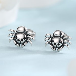 May include: A pair of silver spider stud earrings. The spiders are detailed and have black eyes.