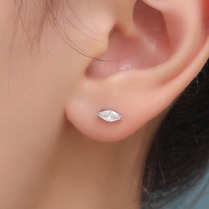 May include: A close-up of a person's ear with a small, silver marquise-shaped stud earring with a clear stone.