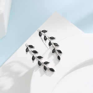 Puede incluir: Un par de pendientes de plata con piedras negras en forma de hoja. Los pendientes están diseñados para parecer una rama con hojas.