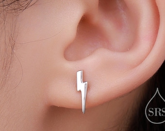 Puede incluir: Un pendiente de plata en forma de rayo. El pendiente se lleva en el lóbulo de la oreja izquierda de una persona con el pelo oscuro.