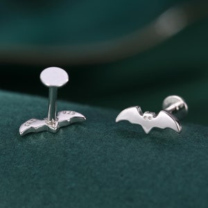 Op de afbeelding: Een paar zilveren oorringen in de vorm van een vleermuis met een pen en een kleine bal aan de bovenkant. De oorringen zijn aan de achterkant gemarkeerd met "925".